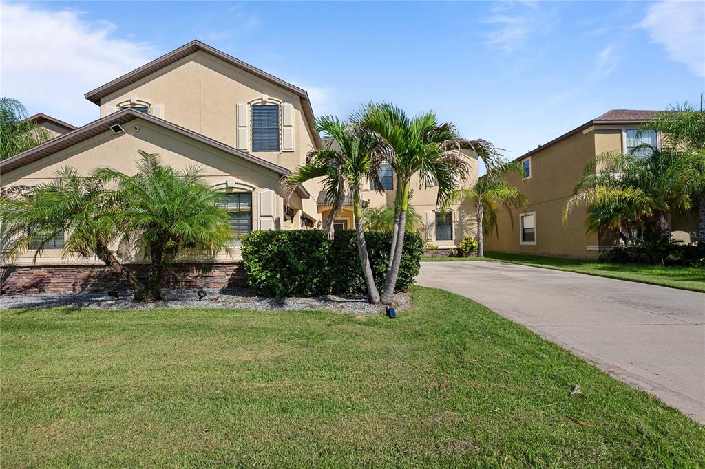A two-story tan stucco house with a stone facade and palm trees in the front — 5049 IVORY STONE DRIVE, WIMAUMA, FL