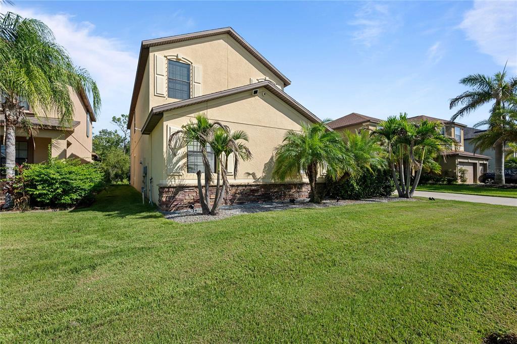 A two-story house with tan stucco siding, stone accents, and palm trees in the yard — 5049 IVORY STONE DRIVE, WIMAUMA, FL