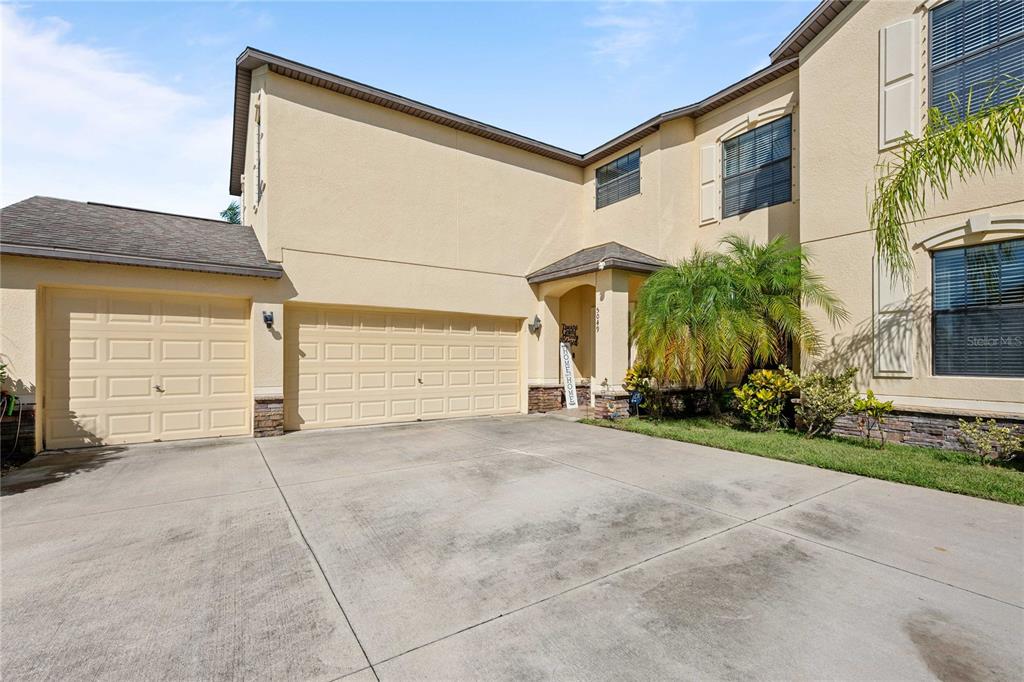 A two-story house with a tan stucco exterior, a three-car garage, and a palm tree — 5049 IVORY STONE DRIVE, WIMAUMA, FL