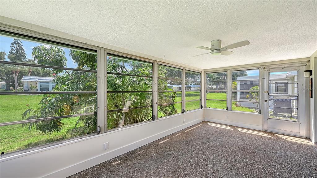 A living room with light wood-look flooring connects to a white kitchen and sliding glass doors — 5911 TIDEWOOD AVENUE UNIT 3, SARASOTA, FL