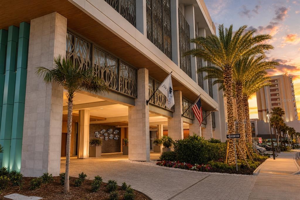 The exterior entrance of a modern hotel building features stone pillars, decorative metal screens, and palm trees — 691 S GULFVIEW BOULEVARD UNIT 711, CLEARWATER, FL