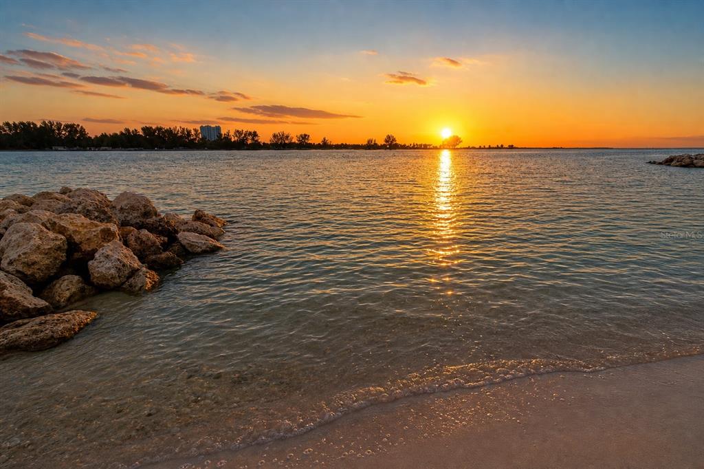 A sunset view over a calm bay with a rocky shoreline and sandy beach — 691 S GULFVIEW BOULEVARD UNIT 711, CLEARWATER, FL