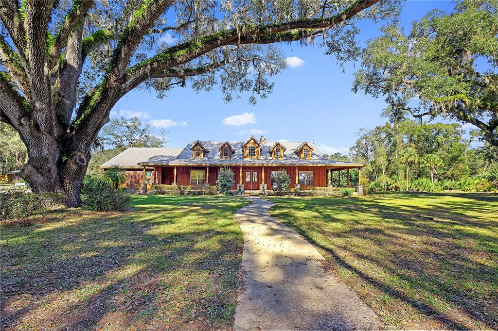 A wooden house with a metal roof sits behind a large oak tree and walkway — 27737 COUNTY ROAD 44A, EUSTIS, FL