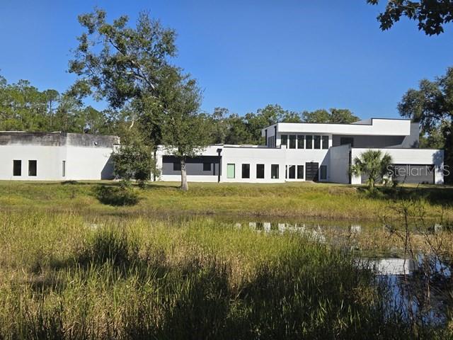 A modern white multi-level house sits behind a grassy pond under a clear blue sky — 2518 SUNSET LANE, LUTZ, FL