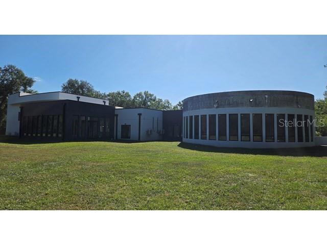 A modern building with a circular section and large windows sits on a grassy lot — 2518 SUNSET LANE, LUTZ, FL