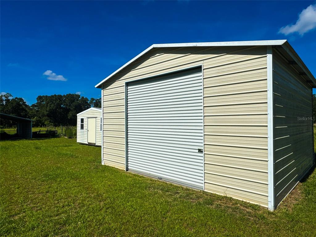 A tan metal storage shed with a roll-up door sits on a grassy lot — 21528 NW 209TH TERRACE, HIGH SPRINGS, FL