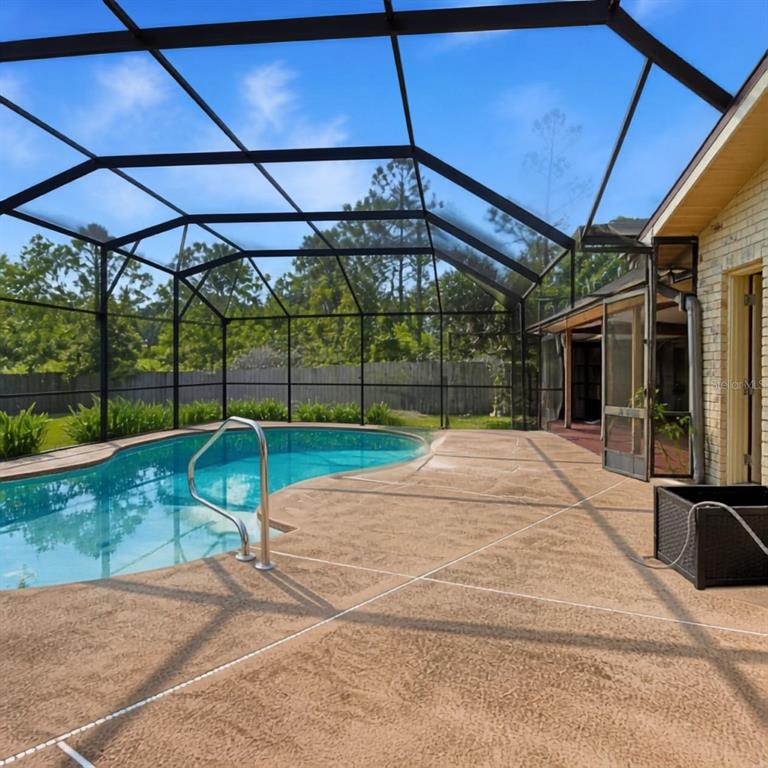 A screened-in pool area features a concrete deck and a kidney-shaped swimming pool — 1004 YALE DRIVE, DELTONA, FL