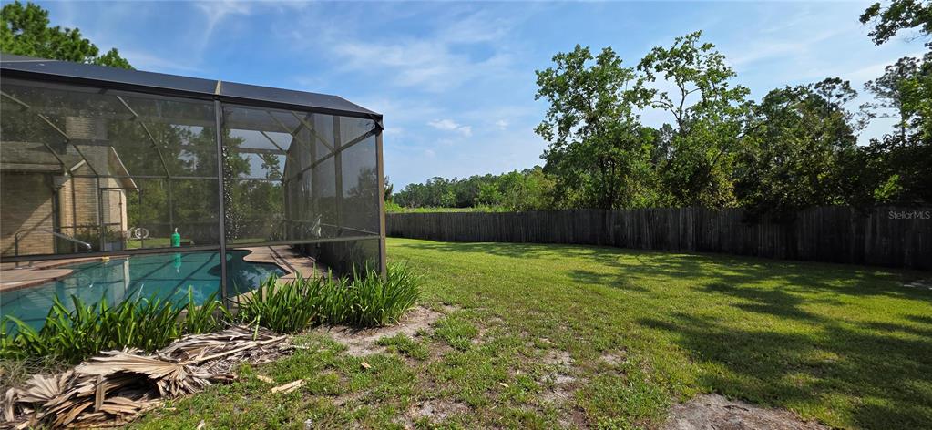 A backyard features a screened-in swimming pool, a grassy lawn, and a wooden privacy fence — 1004 YALE DRIVE, DELTONA, FL