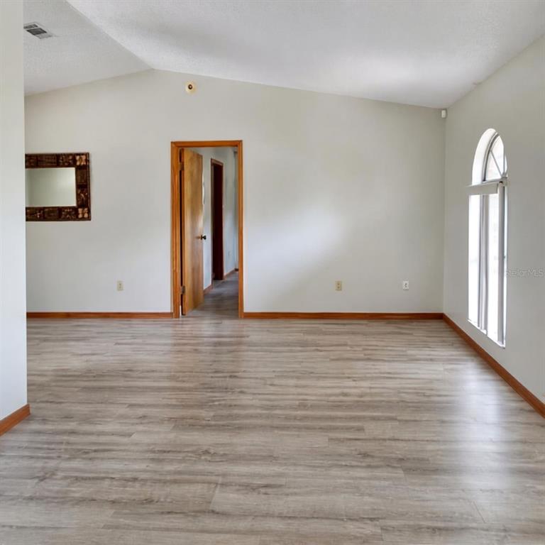 An empty room with light wood-look flooring, a vaulted ceiling, and an arched window — 1004 YALE DRIVE, DELTONA, FL