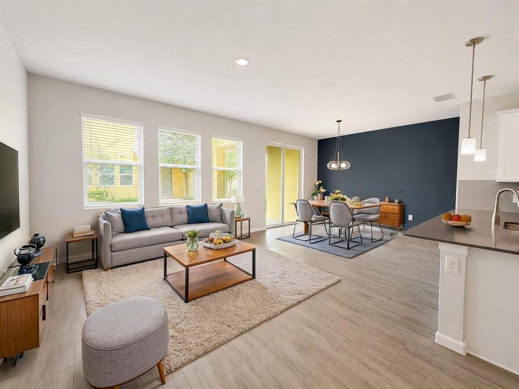 An open-concept living and dining area features light wood-look tile floors and a navy accent wall — 9317 TECUMSEH DRIVE, ORLANDO, FL