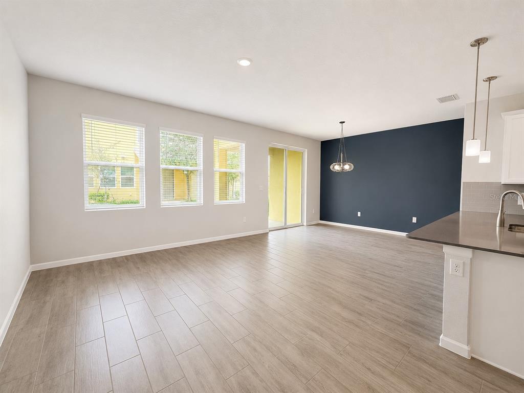 An open-concept living and dining area features light wood-look tile floors and a dark accent wall — 9317 TECUMSEH DRIVE, ORLANDO, FL