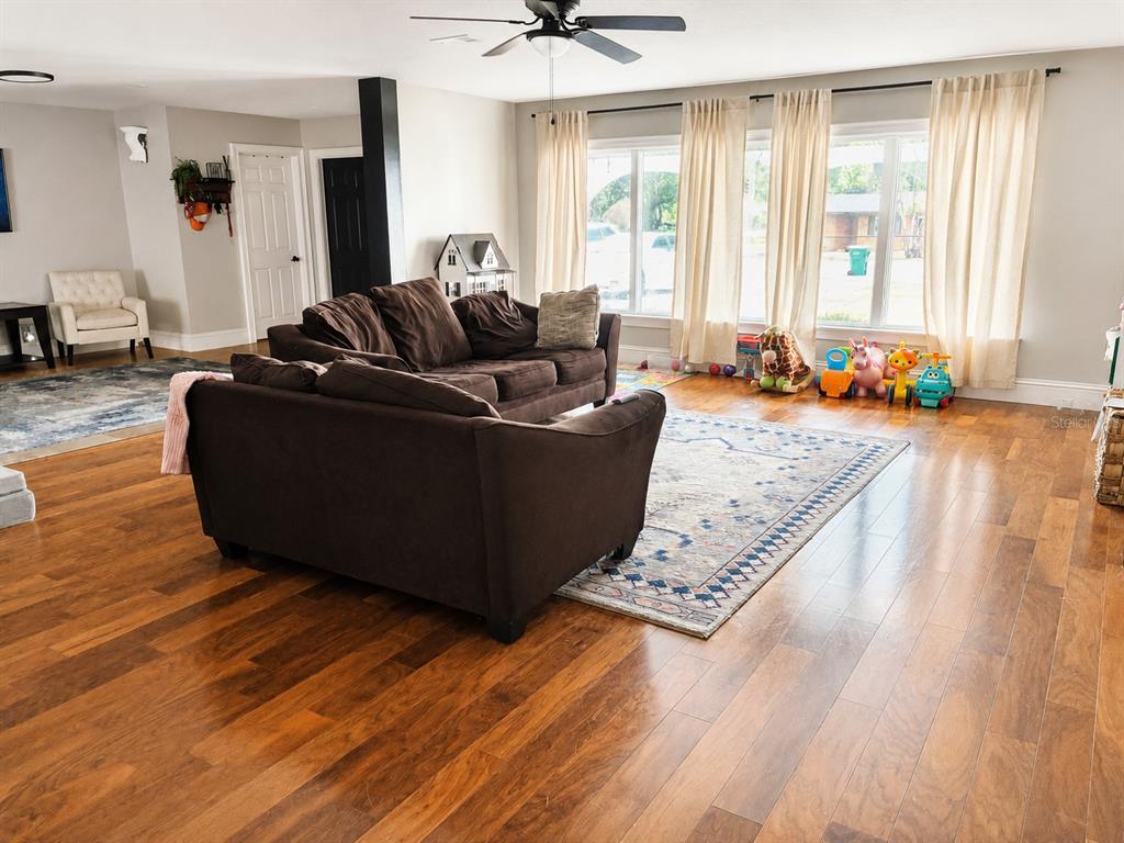 A living room features hardwood floors, a brown sofa, and large windows with light curtains — 12305 LEANNE DRIVE, DADE CITY, FL
