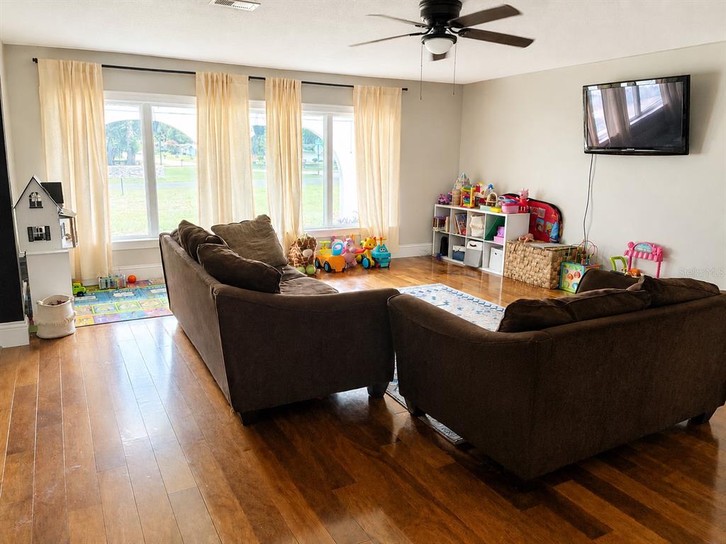 A living room features brown sofas, hardwood floors, large windows with curtains, and children's toys — 12305 LEANNE DRIVE, DADE CITY, FL