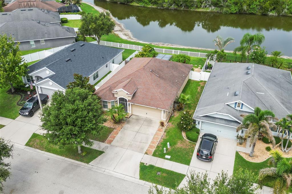 An aerial view shows three suburban houses with driveways and lawns near a small lake — 14358 EDINBURGH MOOR DRIVE, WIMAUMA, FL