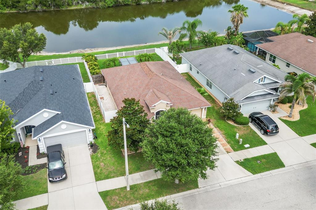 An aerial view shows three suburban houses with driveways and backyards bordering a small lake — 14358 EDINBURGH MOOR DRIVE, WIMAUMA, FL
