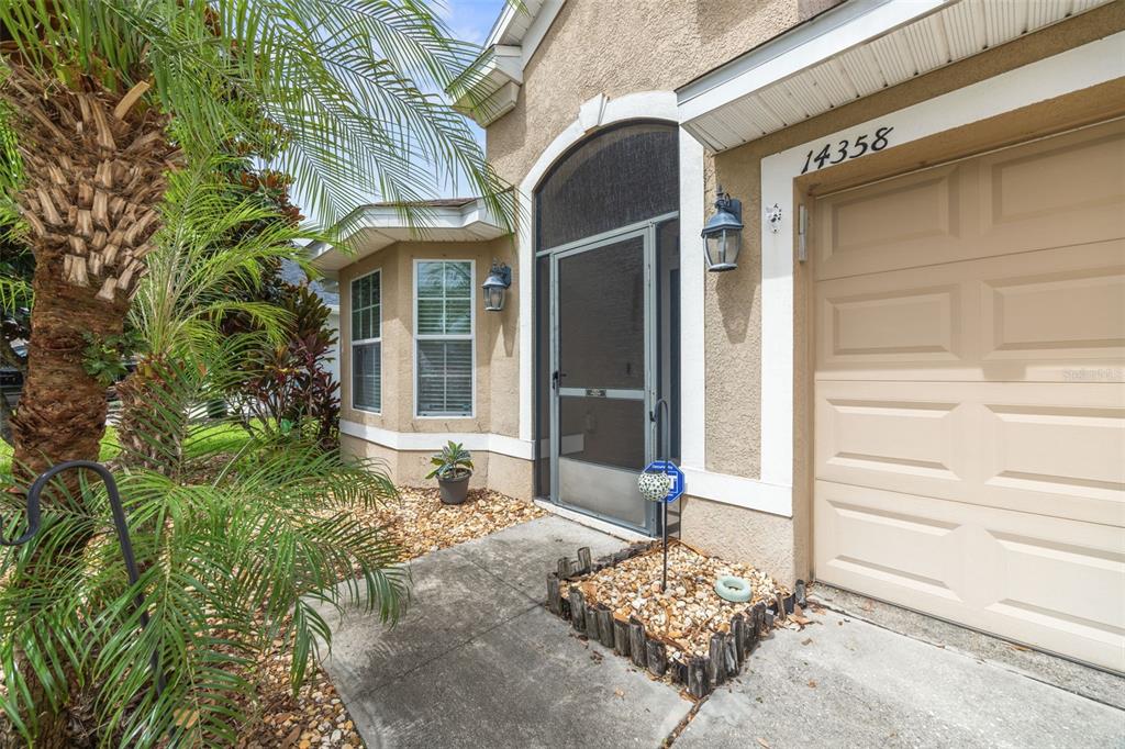 The exterior of a house features a tan stucco facade, a screen door, and landscaping — 14358 EDINBURGH MOOR DRIVE, WIMAUMA, FL