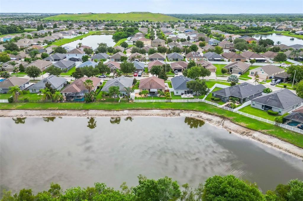 An aerial view shows a suburban neighborhood with houses bordering a large retention pond — 14358 EDINBURGH MOOR DRIVE, WIMAUMA, FL