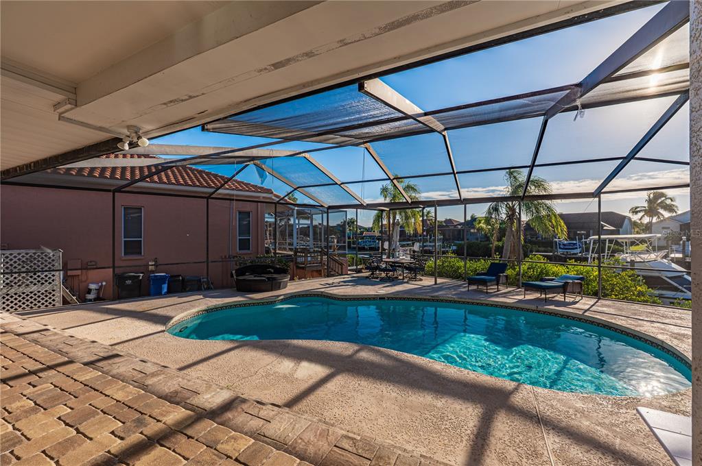 A screened-in pool patio features a kidney-shaped pool, lounge chairs, and a canal view — 930 SYMPHONY ISLES BOULEVARD, APOLLO BEACH, FL