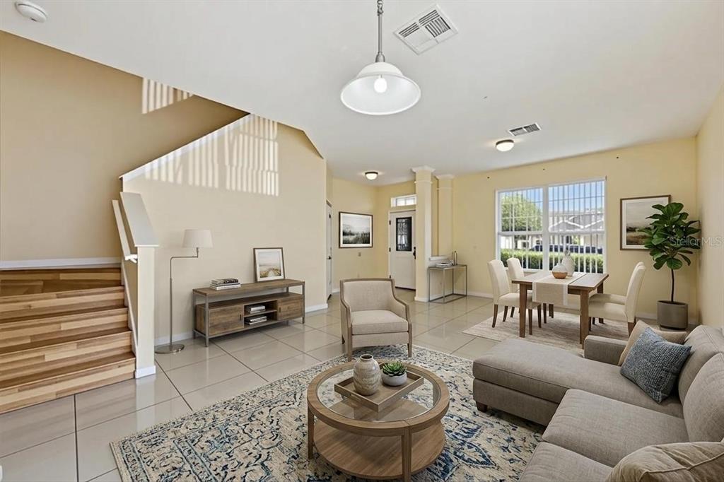 An open-concept living and dining area features light tile floors, a staircase, and neutral furniture — 7613 BEAR CLAW RUN, ORLANDO, FL