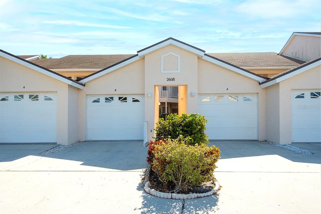 A beige exterior building features three white garage doors and a central landscaped garden bed — 2608 WATERFORD WAY UNIT B, PALMETTO, FL