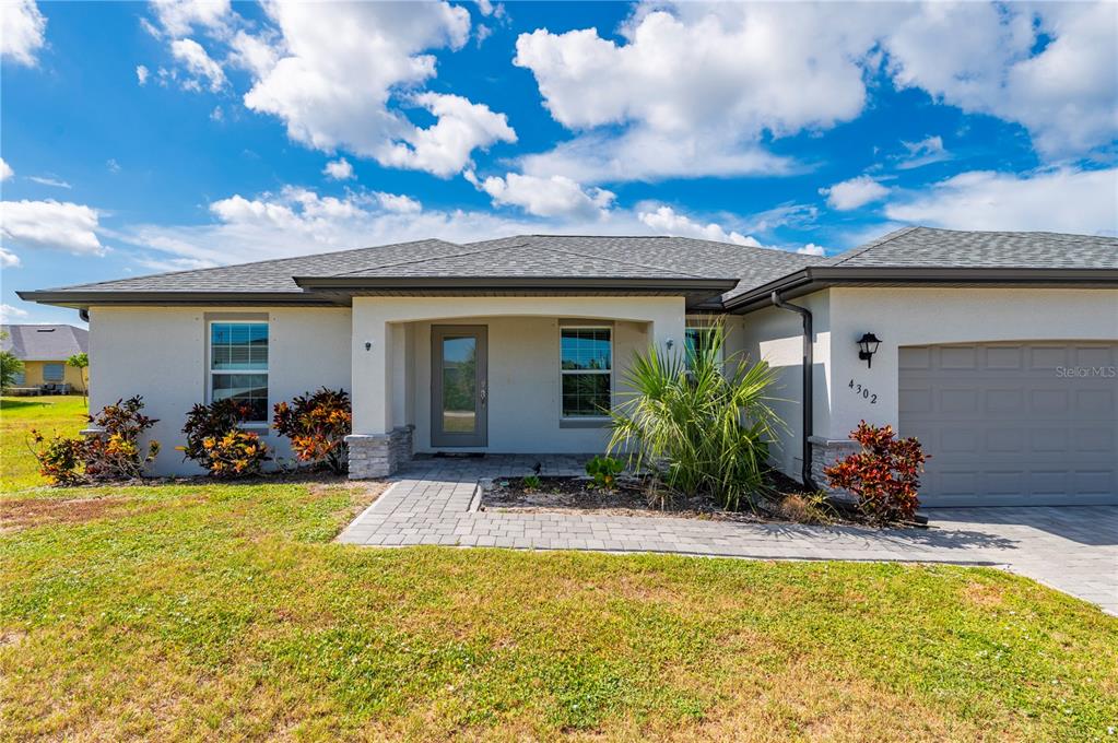 A single-story house with a gray roof, beige stucco walls, and a paved walkway — 4302 NW 32ND STREET, CAPE CORAL, FL