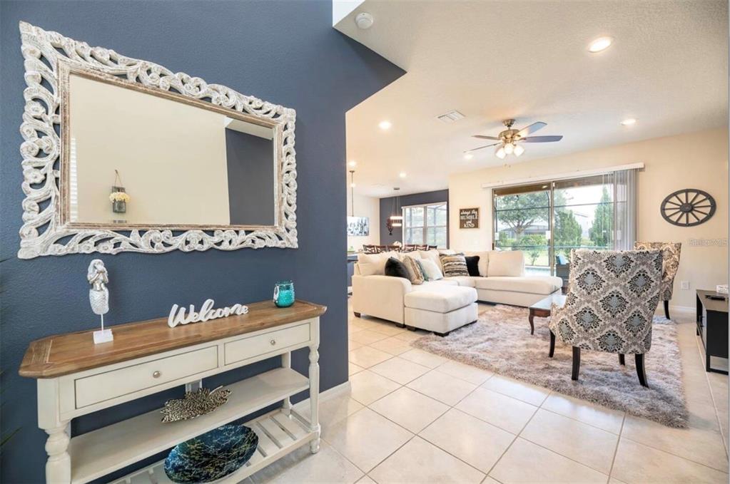 A foyer with a console table and ornate mirror opens into a bright living room — 5533 MISTY OAK CIRCLE, DAVENPORT, FL