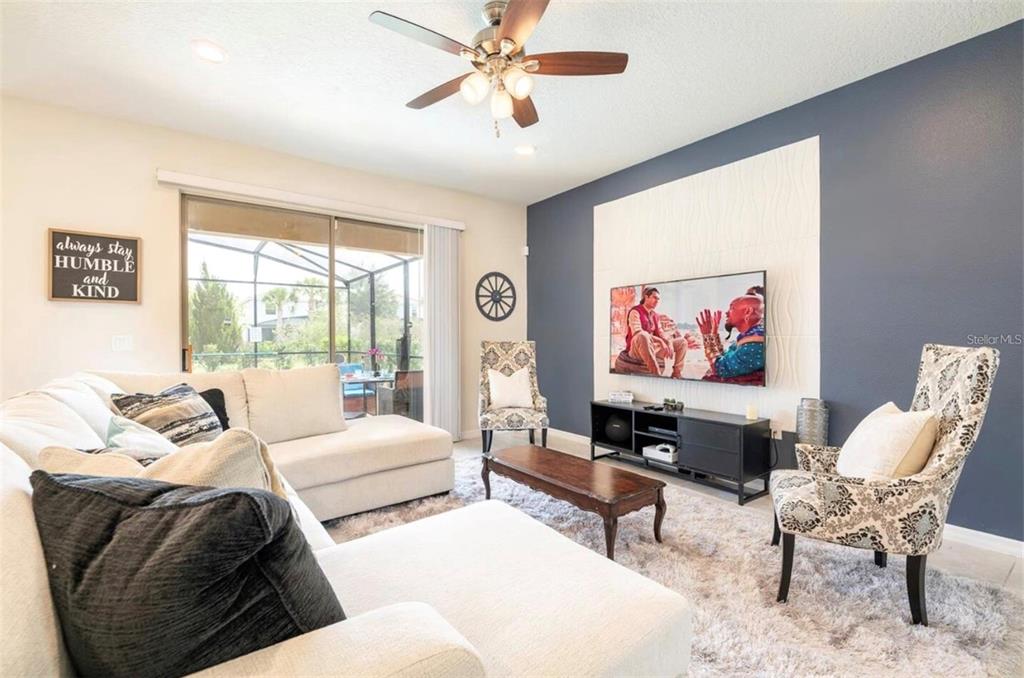 A living room features a white sectional sofa, patterned armchairs, and a wall-mounted television — 5533 MISTY OAK CIRCLE, DAVENPORT, FL