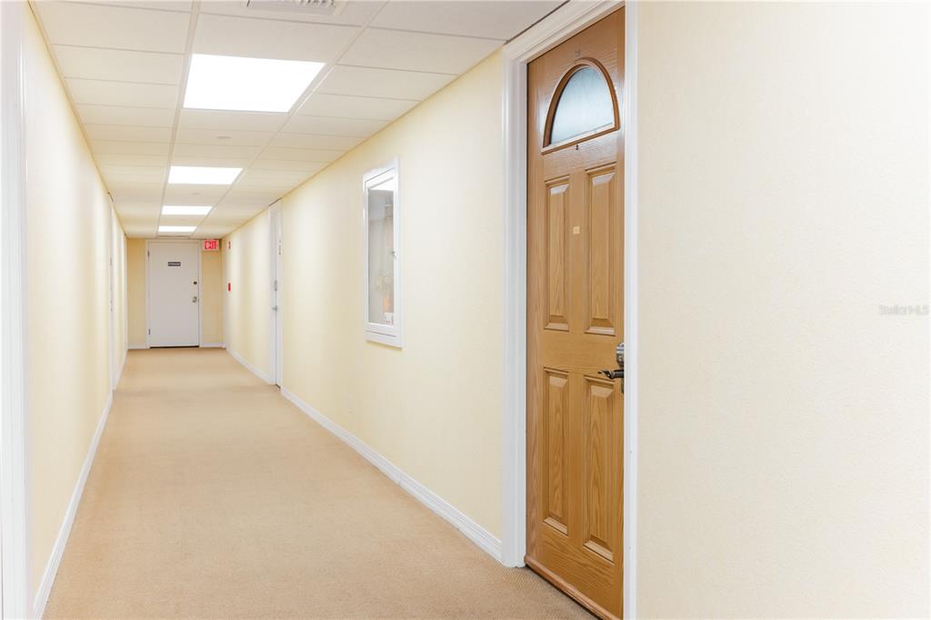 A long, carpeted hallway features light yellow walls, a wooden door, and recessed ceiling lights — 400 64TH AVENUE UNIT 305, ST PETE BEACH, FL