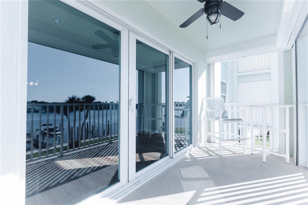 A balcony features white sliding glass doors, a ceiling fan, and a view of water — 400 64TH AVENUE UNIT 305, ST PETE BEACH, FL