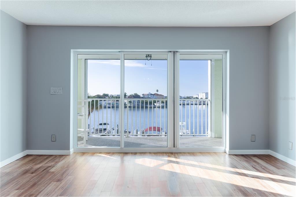 A room with wood-look flooring and sliding glass doors opening to a waterfront balcony view — 400 64TH AVENUE UNIT 305, ST PETE BEACH, FL