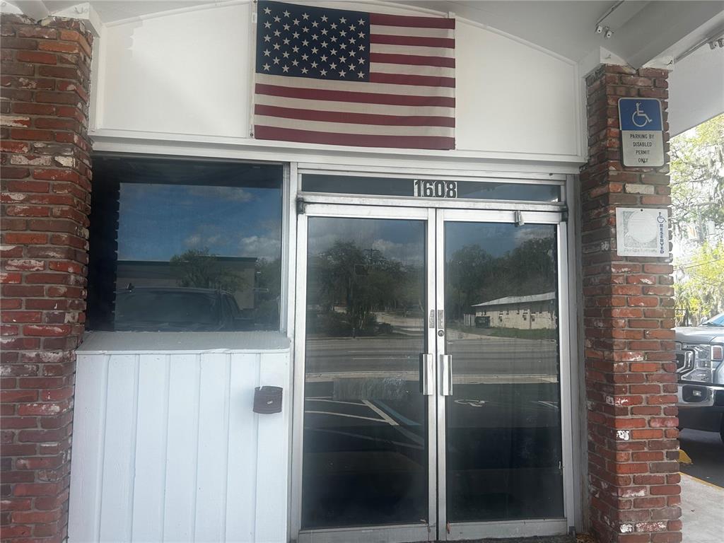 The exterior of a building entrance features a brick facade, glass doors, and an American flag — 1610 S PINE AVENUE, OCALA, FL