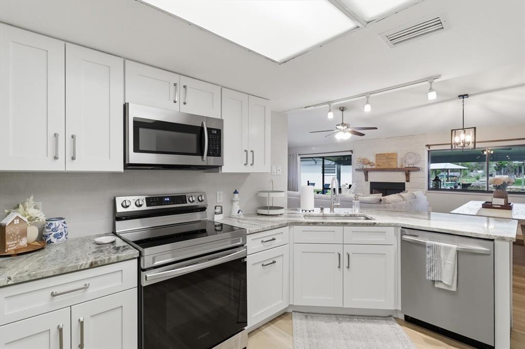 A white kitchen features stainless steel appliances, granite countertops, and an open view into the living room — 11271 W CORAL COURT, CRYSTAL RIVER, FL