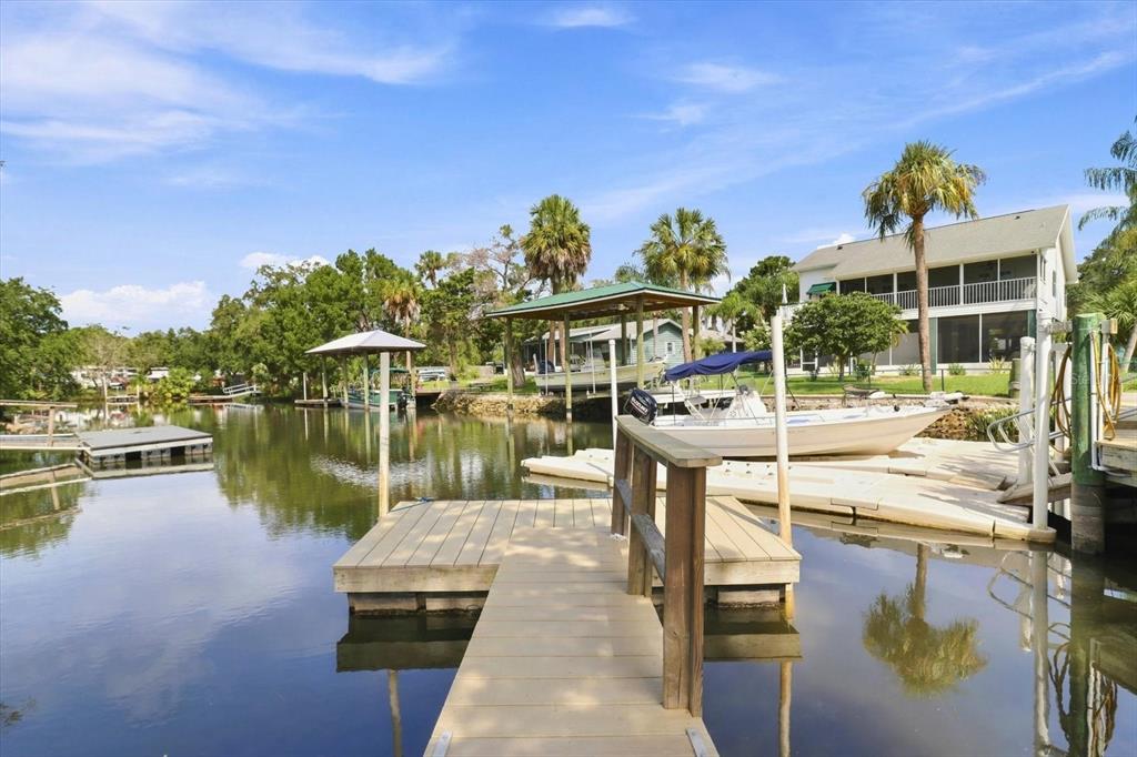 A wooden dock leads to a canal with boat lifts and a house in the background — 11271 W CORAL COURT, CRYSTAL RIVER, FL