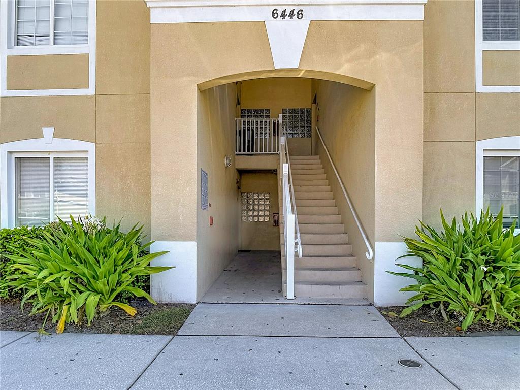 An exterior view of a tan apartment building entrance with stairs leading to an upper level — 6446 CYPRESSDALE DRIVE UNIT 202, RIVERVIEW, FL