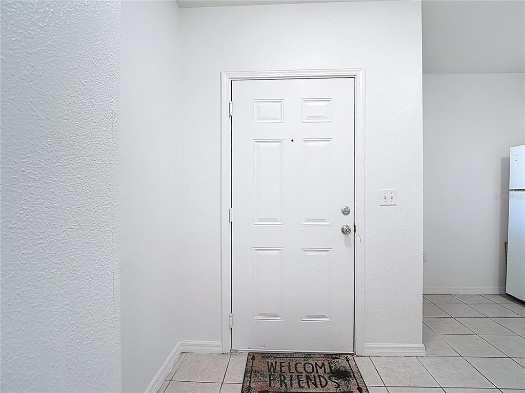 A white front door with a welcome mat sits in a tiled entryway — 6446 CYPRESSDALE DRIVE UNIT 202, RIVERVIEW, FL