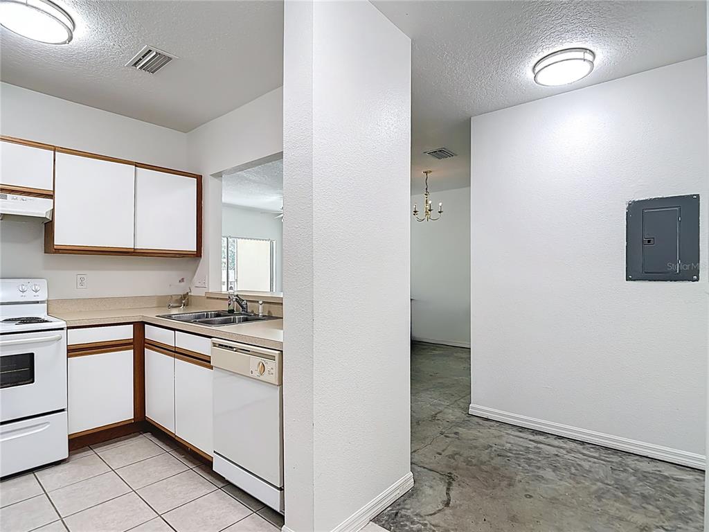 A kitchen with white cabinets and tile flooring opens into a dining area — 6446 CYPRESSDALE DRIVE UNIT 202, RIVERVIEW, FL