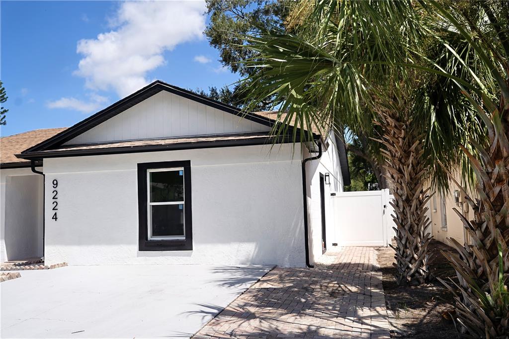A white house with black trim features a concrete driveway and a brick walkway — 9224 CAMINO VILLA BOULEVARD, TAMPA, FL