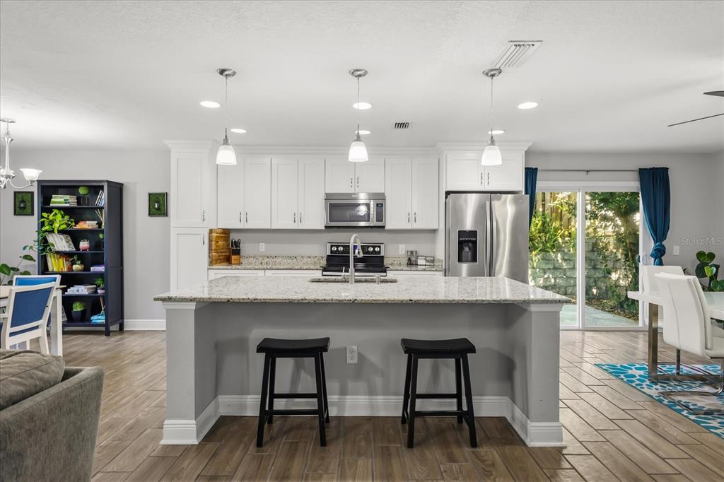A kitchen features white cabinetry, granite countertops, a central island with bar stools, and stainless appliances — 524 E HILLCREST STREET, ALTAMONTE SPRINGS, FL