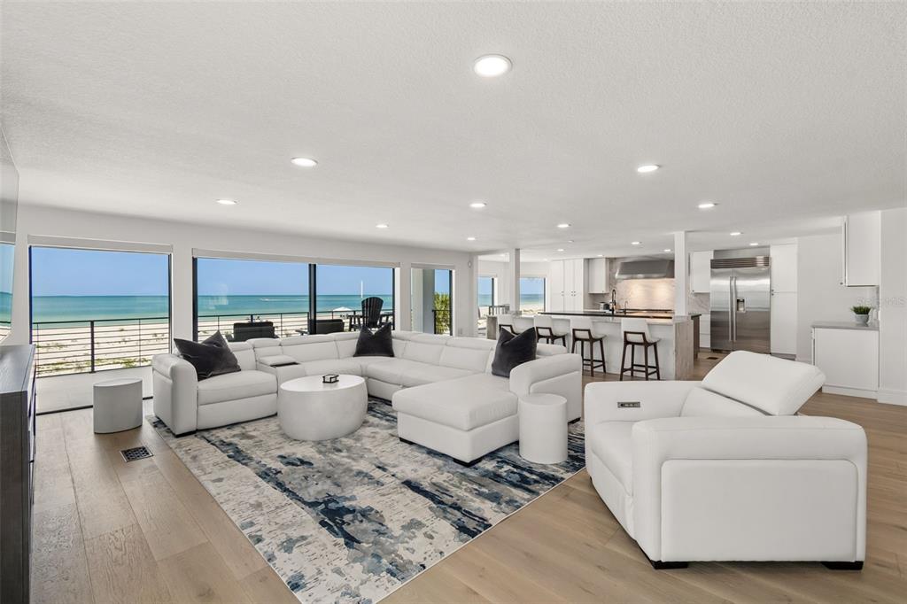 A bright, open-concept living room and kitchen featuring white furniture, hardwood floors, and ocean views — 930 ELDORADO AVENUE, CLEARWATER BEACH, FL