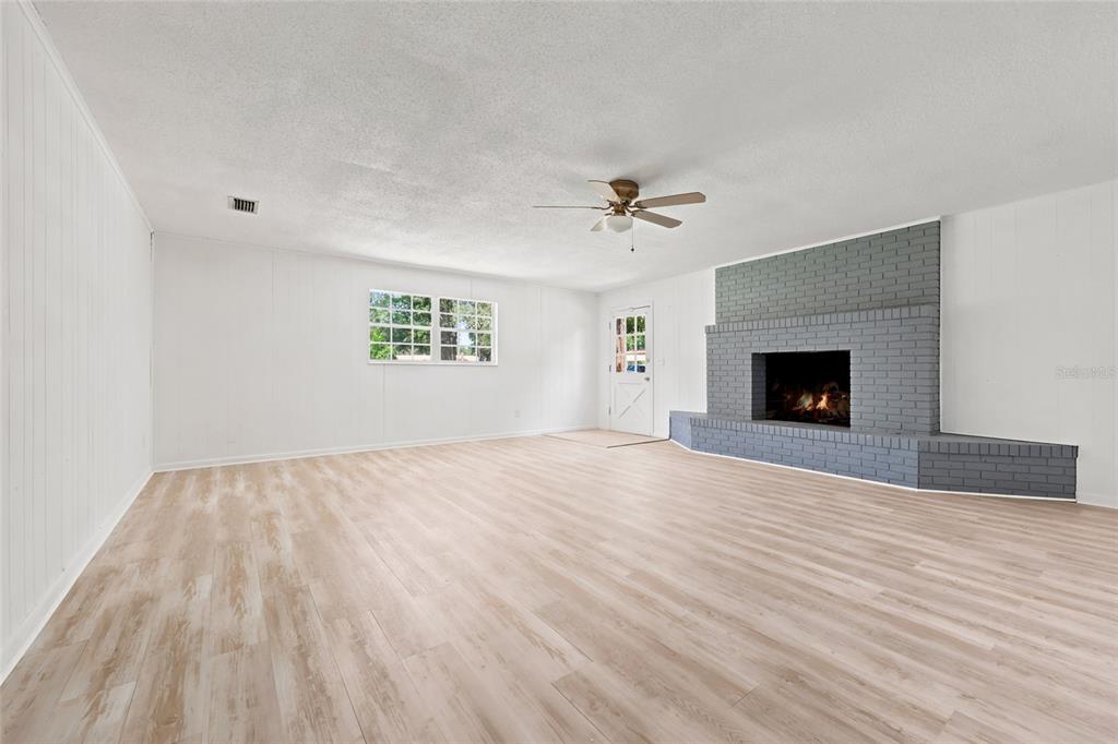 A spacious living room features light wood-look flooring, white walls, and a gray brick fireplace — 167 SW THURMAN TERRACE, LAKE CITY, FL