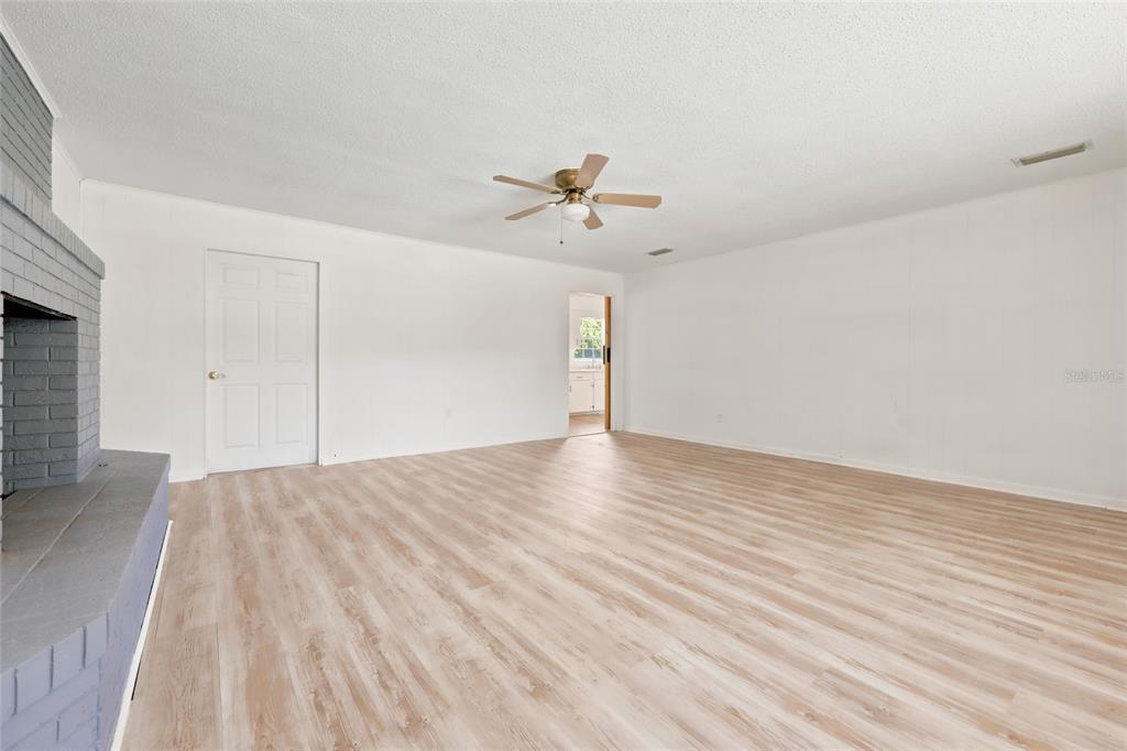 A living room features light wood-look flooring, white walls, a ceiling fan, and a brick fireplace — 167 SW THURMAN TERRACE, LAKE CITY, FL