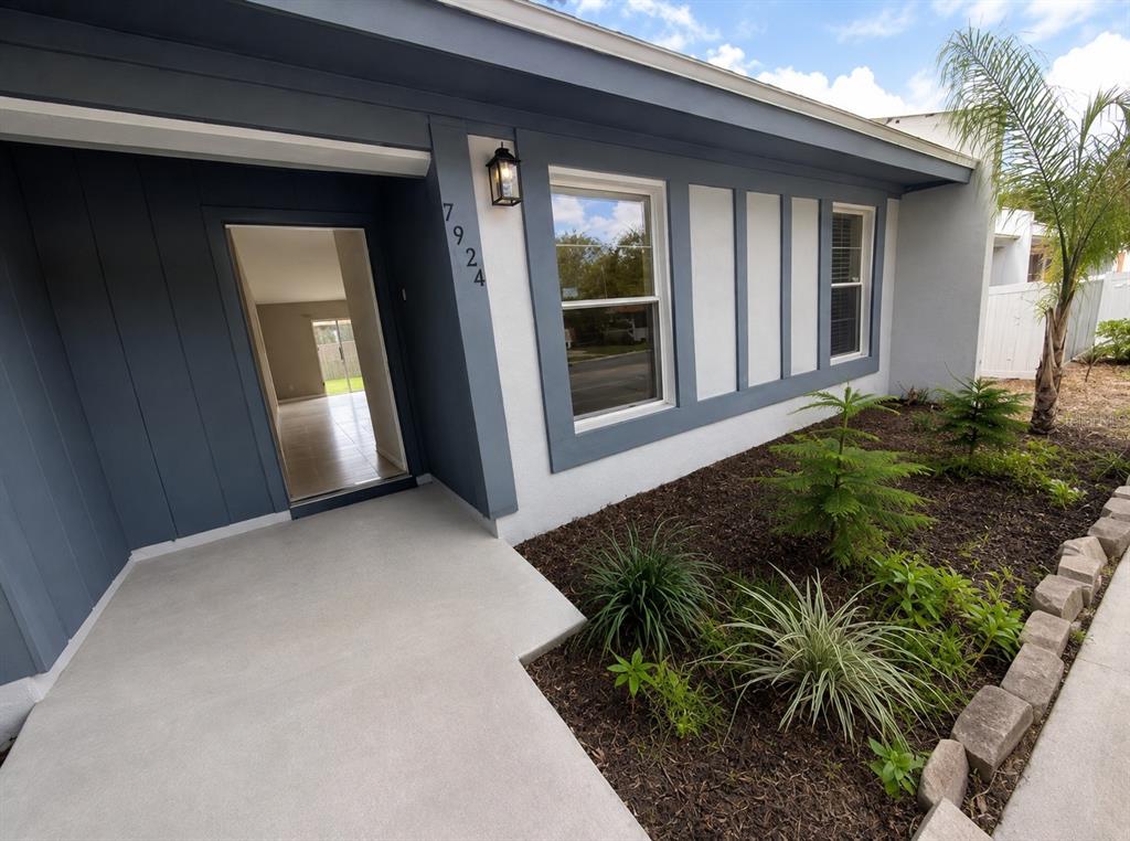 The exterior of a house features a blue-trimmed entrance, a concrete porch, and landscaped garden beds — 7924 GUARDSMEN STREET, ORLANDO, FL