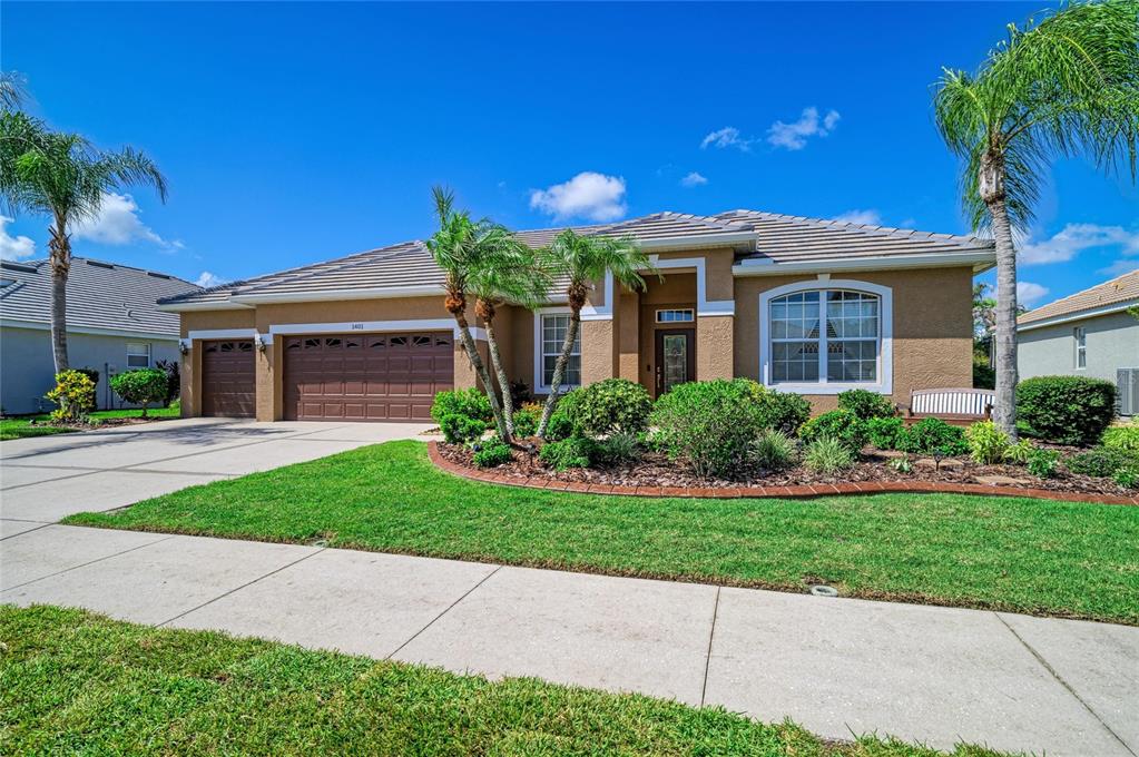 A single-story house with a brown tile roof, tan stucco exterior, and a two-car garage — 1401 PINYON PINE DRIVE, SARASOTA, FL