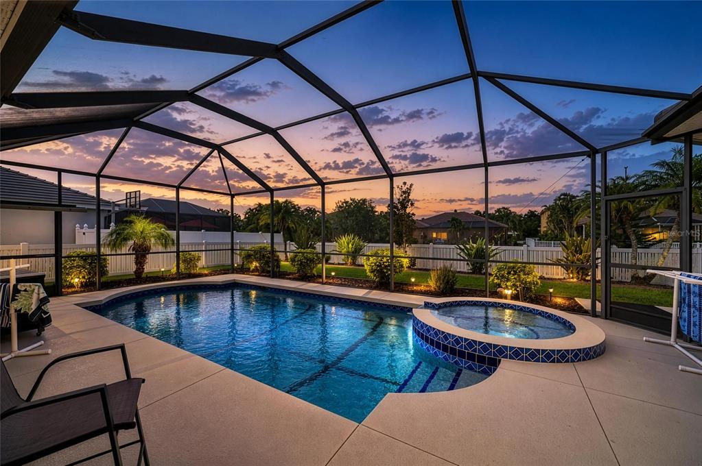 A screened-in swimming pool and hot tub at sunset with a white fence in the background — 1401 PINYON PINE DRIVE, SARASOTA, FL