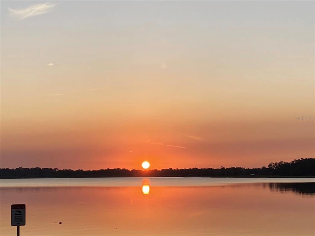 A sunset over a calm lake with a small warning sign in the foreground — 7820 TWITTY ROAD, SEBRING, FL