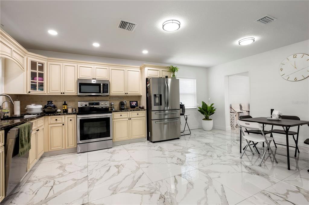 A kitchen features cream-colored cabinets, stainless steel appliances, and white marble-patterned tile flooring — 2811 W OHIO AVENUE, TAMPA, FL