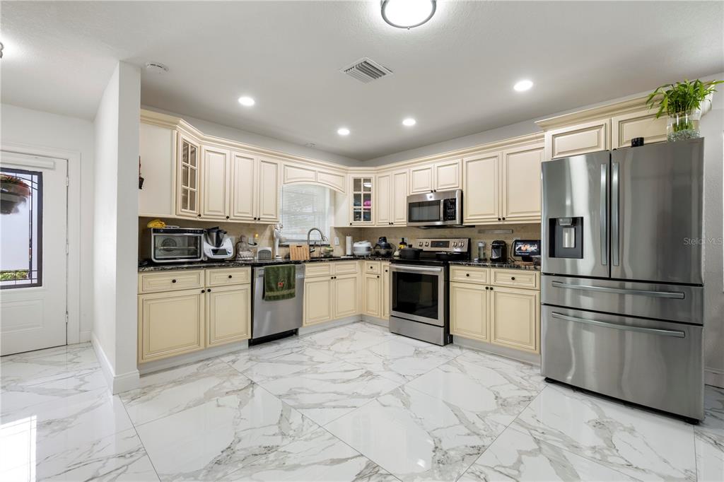 A kitchen features cream-colored cabinets, stainless steel appliances, and white marble-patterned tile flooring — 2811 W OHIO AVENUE, TAMPA, FL