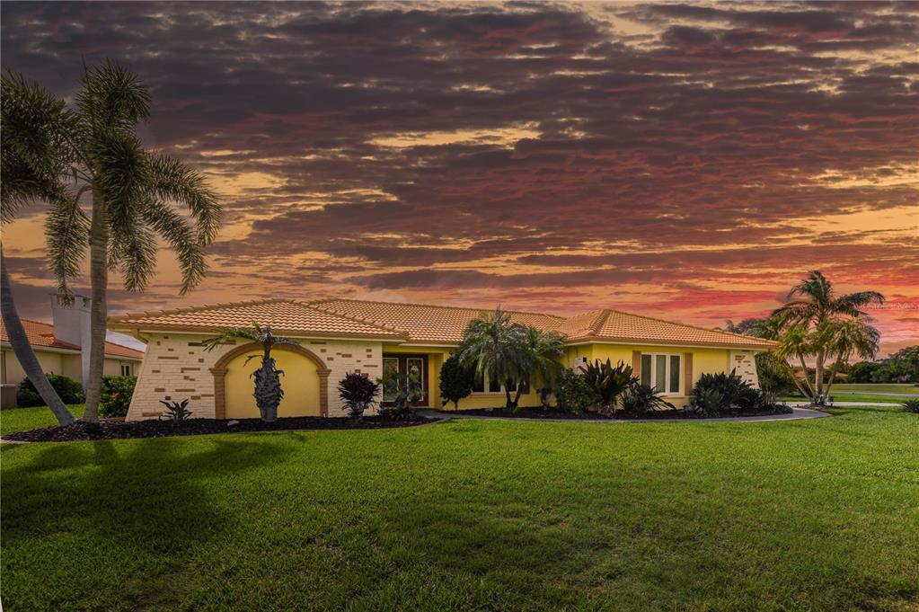 A yellow single-story house with a tile roof and palm trees under a sunset sky — 1800 LIESL DRIVE E, VENICE, FL
