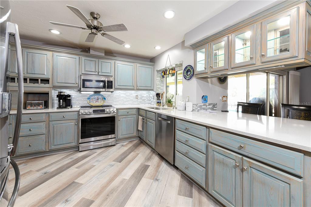 A kitchen features light blue distressed cabinets, stainless steel appliances, and white quartz countertops — 1800 LIESL DRIVE E, VENICE, FL
