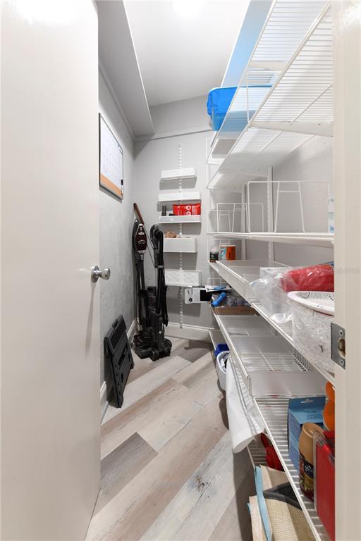 A narrow pantry features white wire shelving, light wood-look flooring, and a wall-mounted vacuum cleaner — 1800 LIESL DRIVE E, VENICE, FL
